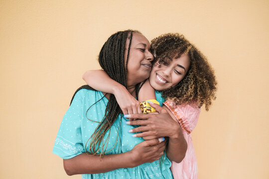 Cheerful african mother and adult daughter hugging each other while wearing traditional dress