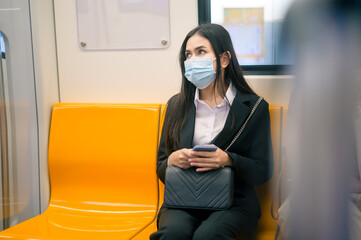 Young business woman with face mask  is standing on metro platform using smart.