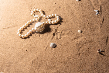 Shells and pearl necklace on the beach sand, selective focus.