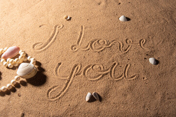Shells and pearl necklace on the beach sand with romantic phrases written in the sand, selective focus.