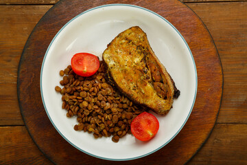 A plate of fish with lentils and tomatoes on a wooden table.