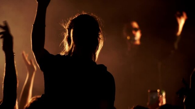 Woman sits at someone's shoulders and listens to singer at scene in night club. Lady waves her hand to the beat. There is music concert in slow motion. Spectators are dancing and listening to vocalist