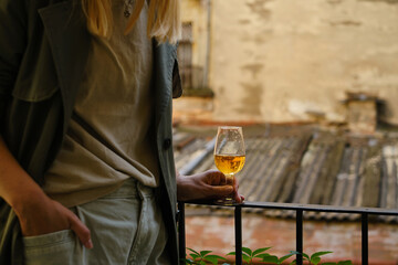 Beautiful girl with a wine glass on the balcony. Drinks white wine and enjoy the moment. A celebration holiday alone. Relaxed lifestyle. Happy woman rest after work. Beautiful European courtyard