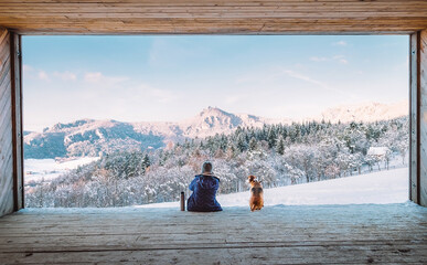 Woman with thermos flask sitting with her beagle dog in the big wooden hangar with a huge panoramic...