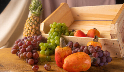 Grapes in a wooden box and cashews and pineapple with fabrics in the background and rustic wood, low depth of field, selective focus.