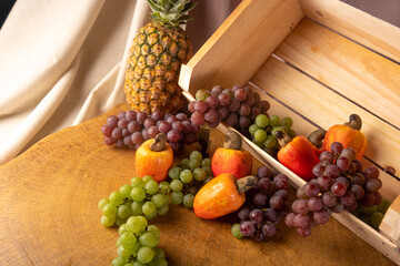 Grapes in a wooden box and cashews and pineapple with fabrics in the background and rustic wood, low depth of field, selective focus.