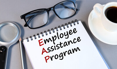 EMPLOYEE ASSISTANCE PROGRAM, text on white notepad paper on a gray background near a magnifying glass and a CUP OF COFFEE