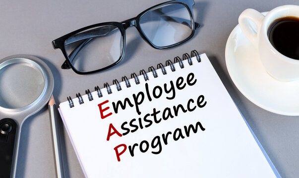 EMPLOYEE ASSISTANCE PROGRAM, text on white notepad paper on a gray background near a magnifying glass and a CUP OF COFFEE