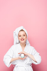 happy young woman in bathrobe with towel on head holding deodorant on pink.