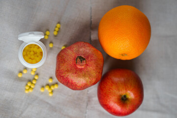 Apple, pomegranate and orange lie on a gray canvas and next to them scattered vitamins from jars