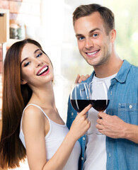 Portrait of young couple drinking redwine, at home. Caucasian models with red wine glasses in love concept. Happy man and woman posing together indoors.
