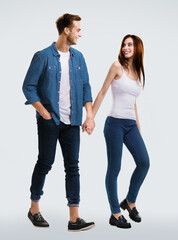 Fototapeta premium Happy lovers concept - young couple walking together, going somewhere, holding hands. Bright grey background. Caucasian models at full body length studio portrait image. Man and woman.