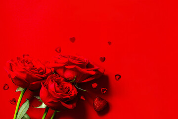 Red roses and heart shaped decor on a red background. Copy space for your design or message.