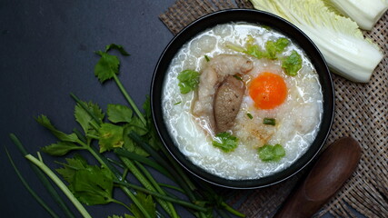 Congee with minced pork and boiled egg in black bowl on a dark background