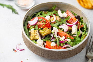 Eggplant salad with tomatoes, arugula and feta cheese in a bowl on white background