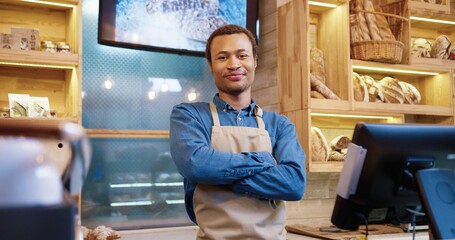 Close up portrait of joyful handsome African American man seller in face mask standing in bakery shop, looking at camera in good mood at workplace. Bakehouse owner. small business. Work concept