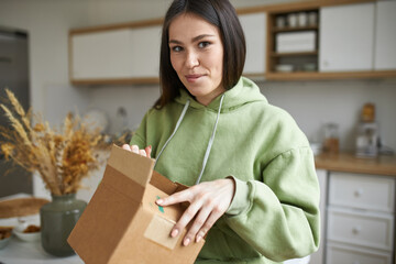 Portrait of excited joyful young female with dark hair holding opening cardboard box, receiving...