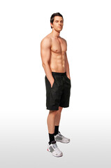 Portrait of a fit young white male athlete with short dark hair posing by himself with hands in his black short pockets in a studio with a white background.