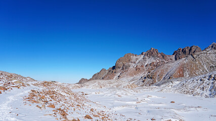 High rocks covered with snow. The Tuyuk Su Glacier. The view from the drone to the tops of the peaks. Completely surrounded by winter mountains. blue clear sky and bright sun. Shadows from mountains