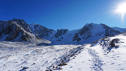 High rocks covered with snow. The Tuyuk Su Glacier. The view from the drone to the tops of the peaks. Completely surrounded by winter mountains. blue clear sky and bright sun. Shadows from mountains