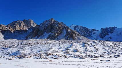 High rocks covered with snow. The Tuyuk Su Glacier. The view from the drone to the tops of the peaks. Completely surrounded by winter mountains. blue clear sky and bright sun. Shadows from mountains