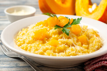 Pumpkin risotto with parmesan cheese and parsley in plate on wooden background