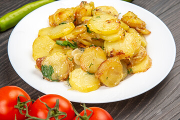 cooked fried potatoes with herbs and vegetables in a white plate on a wooden table