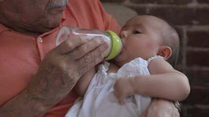 Hispanic grandfather holding and feeding a newborn baby granddaughter with a bottle