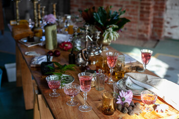 a variety of crystal glasses with rose wine, plates, candlesticks and other vintage staff in a mess on a wooden table
