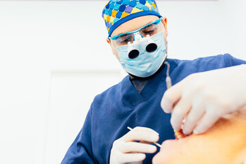 Male dentist with glasses and cap performs surgery on the patient's mouth at the clinic. Copy space.