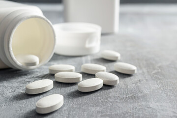 White pills and bottle on textured grey background, medicines, antibiotic, calcium, painkiller, vitamin supplements close-up view