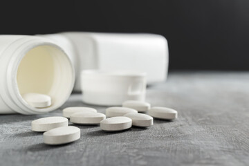 White pills and bottle on textured grey background, medicines, antibiotic, calcium, painkiller, vitamin supplements close-up view