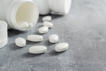 Fototapeta na wymiar White pills and bottle on textured grey background, medicines, antibiotic, calcium, painkiller, vitamin supplements close-up view