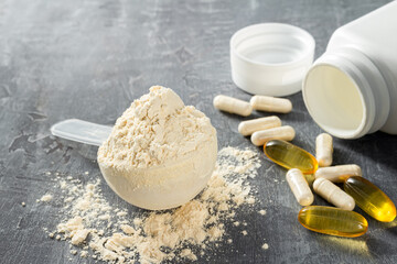 Scoop of whey or soy protein isolate, omega-3 capsules, white pills of bcaa, beta-alanine and...