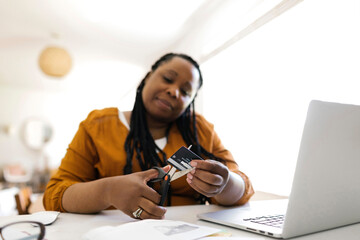 Woman cutting credit card with scissors while working in home office