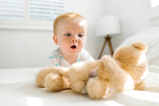 Baby boy (6-11 months) looking at teddy bear on bed
