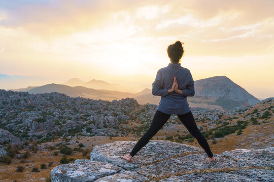 Full body back view of unrecognizable barefoot female standing in Star pose with reverse prayer hands on top of mountain while practicing yoga in nature at sunset time