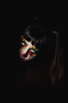 Creepy Female With Painted Face And In Contact Lenses Peeping Out Of Darkens At Night On Halloween