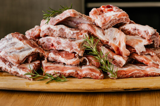 Heap of uncooked meat ribs with fat and aromatic rosemary sprigs on wooden table