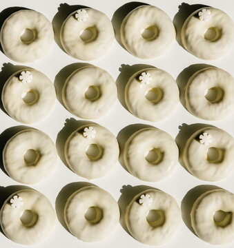 Overhead view of tasty doughnuts decorated with icing sugar glaze and flowers on white background