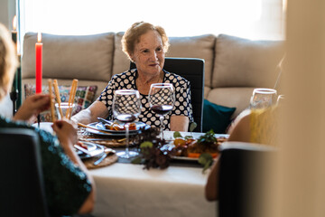 Cheerful senior women at table with tasty food and alcoholic beverages during festive event in flat