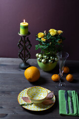 Christmas still life with yellow plate with golden leaves, wine glass, cutlery, decorated rose bush, burning candle, orange, tangerine on brown background