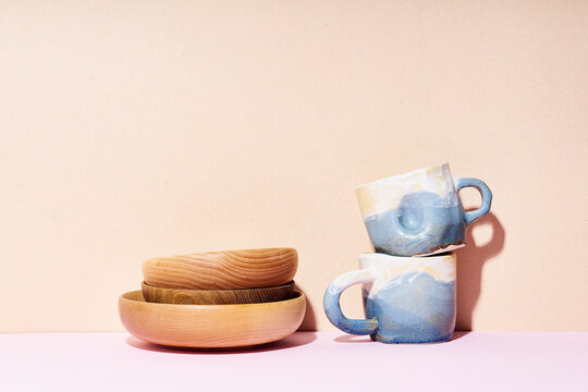 Still life with handmade ceramic cups and wooden bowls on bright studio