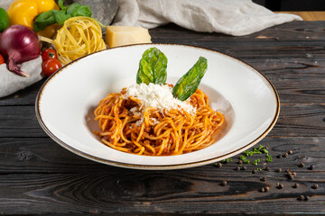Bolognese pasta with cheese and herbs. A hot main course of spaghetti, minced meat, tomato paste, parmesan cheese and basil in a ceramic plate on a wooden kitchen table.