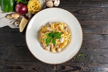 Tagliatelle with chicken and mushrooms. Hot main course of pasta, chicken fillet, mushrooms, cheese, French mustard, sauce and parsley in a ceramic plate on a wooden kitchen table.