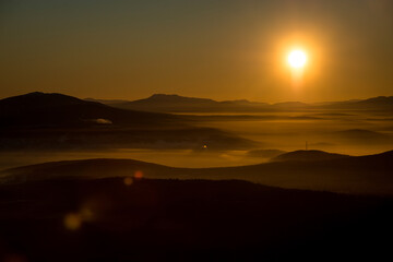 the sun sets below the horizon and illuminates the fog in the valley with a yellow light