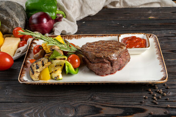 Filet mignon steak with grilled vegetables. A hot main course of beef or veal with corn, eggplant, cherry tomatoes, bell peppers, rosemary and ketchup or barbecue sauce.