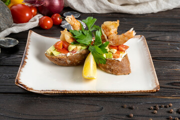 Bruschetta with shrimps, vegetables and herbs. Cold appetizer of bread, avocado, tomato, shrimp and greens with lemon in a ceramic plate on a wooden kitchen table.