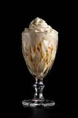 Classic milkshake with banana, caramel and whipped cream in a glass on a black background. Protein sweet cocktail. Cold drink.