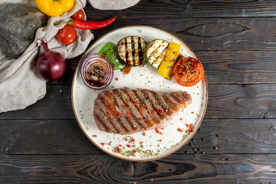 Rib Eye Steak With Grilled Vegetables. A Classic Hot Dish Of Premium Beef Steak (cowboy Ribeye Or Entrecote) With Eggplant, Zucchini, Peppers, Tomatoes And Onions On A Wooden Kitchen Table.